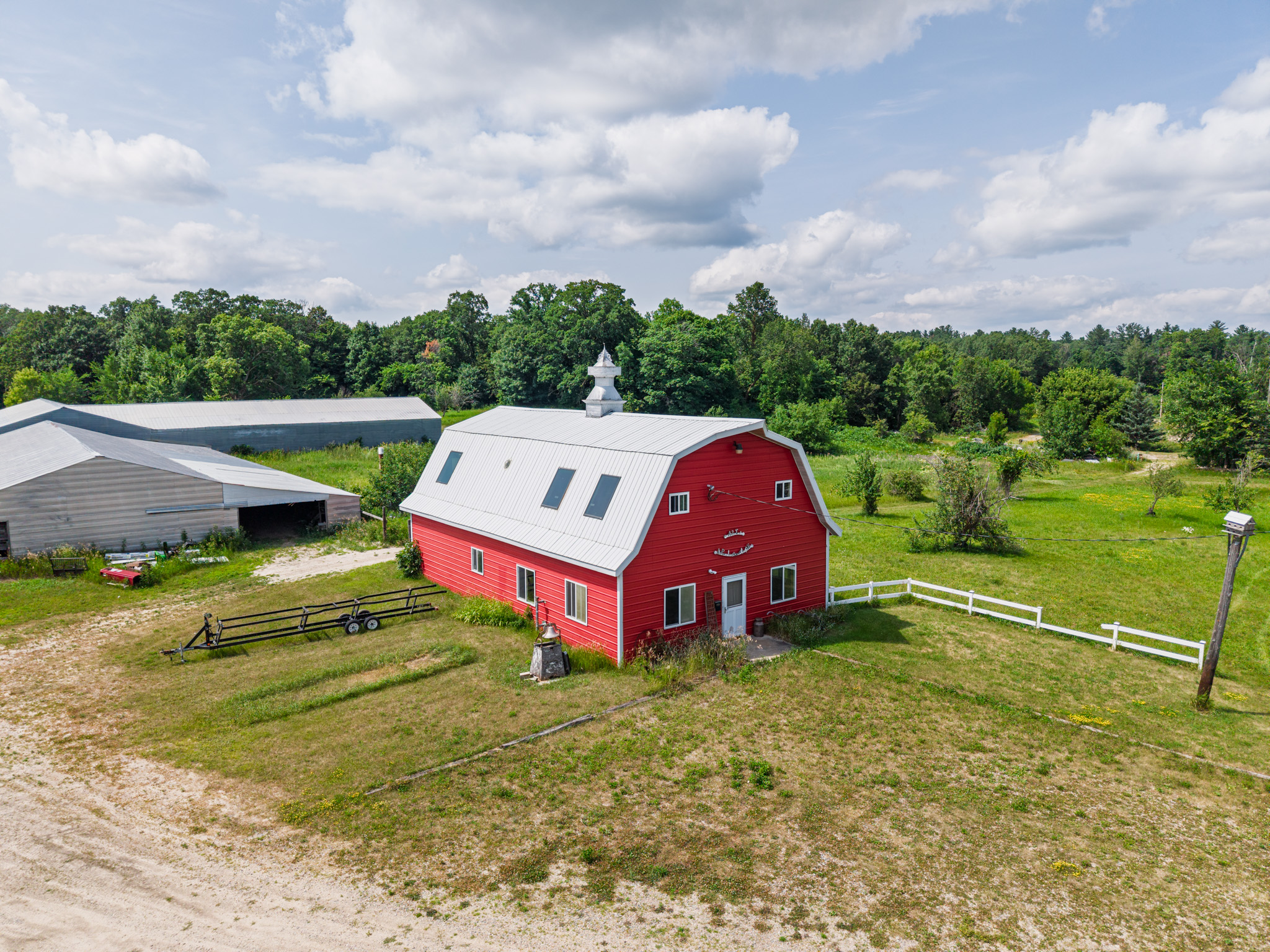 Elevated aerial view of a red barn, outbuildings, fencing, and surrounding acreage