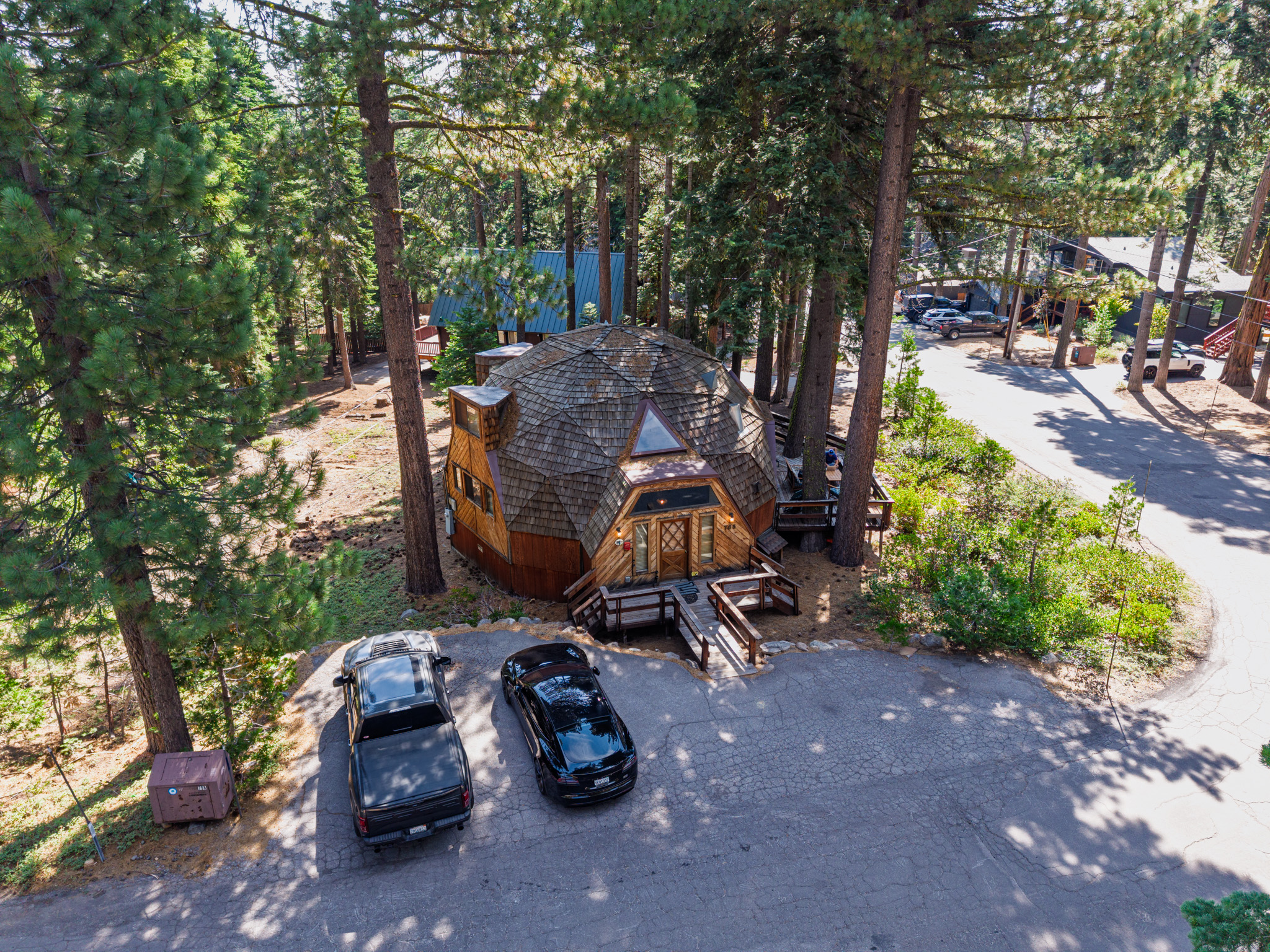 Front aerial view of a round wooden cabin and its entry among tall pine trees