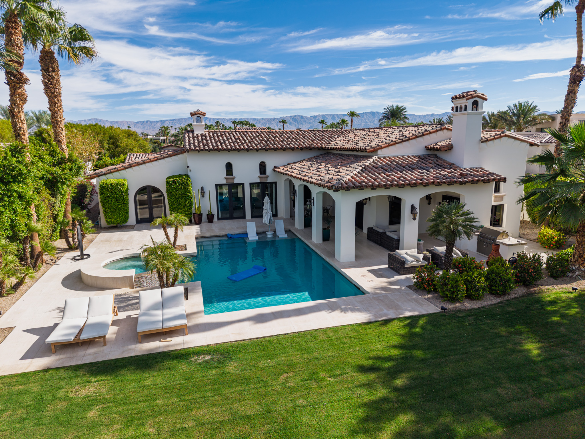 Aerial view of a desert estate with its pool, spa, covered patio, and mountain backdrop